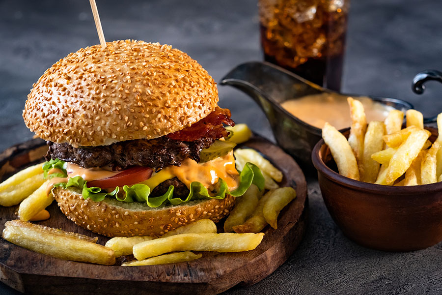 Fresh burger with crispy french fries near beverage and sauce boat